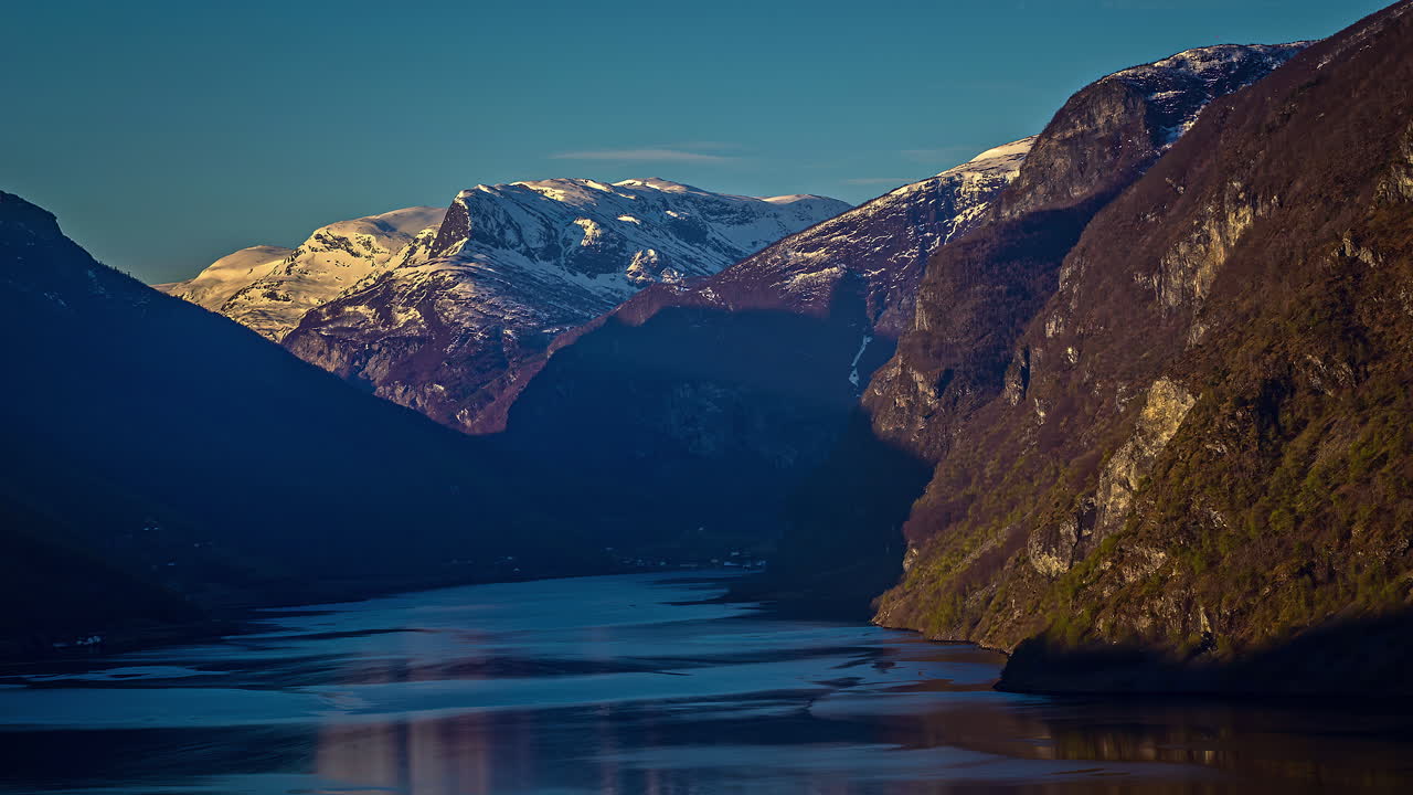 Splendida e tranquilla acqua del fiordo circondata da montagne innevate illuminate dall'alba in Norvegia - Ripresa grandangolare in timelapse.