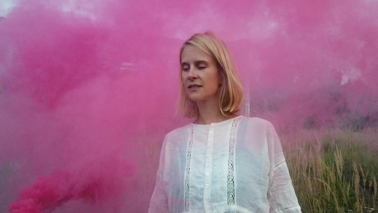 Incredibile ripresa cinematografica al rallentatore di una ragazza bionda solitaria e inquietante in abito bianco, solo con un fumogeno rosso in una sala carri armati. Servizio fotografico/video in luoghi abbandonati nella natura 1080, 24p di Philipp Marnitz
