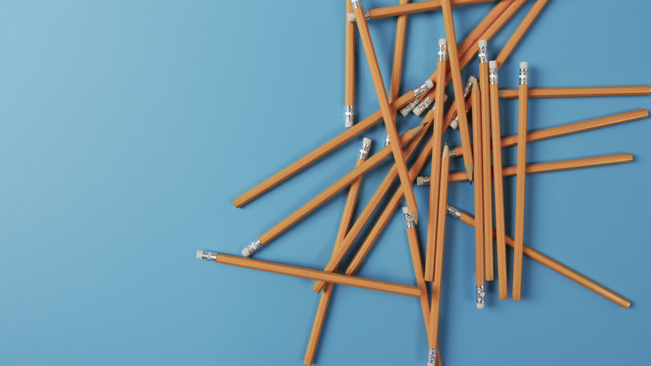 A collection of yellow pencils with erasers is scattered across a blue background, with copy space