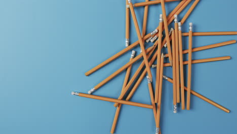 a collection of yellow pencils with erasers is scattered across a blue background, with copy space