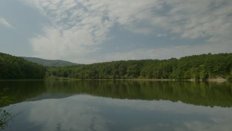 Calm-lake-with-cloud-reflections-in-scenic-landscape-pan-down-shot