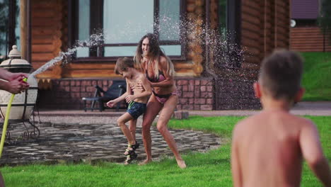 happy family with two kids playing with garden hose pouring water on grass