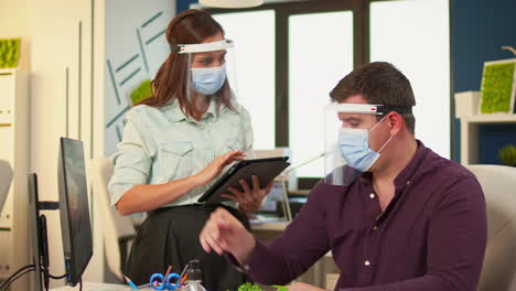 employees with protection masks discussing looking at computer