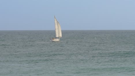 a sailboat with a white sail at sea moving away from the sea to the right