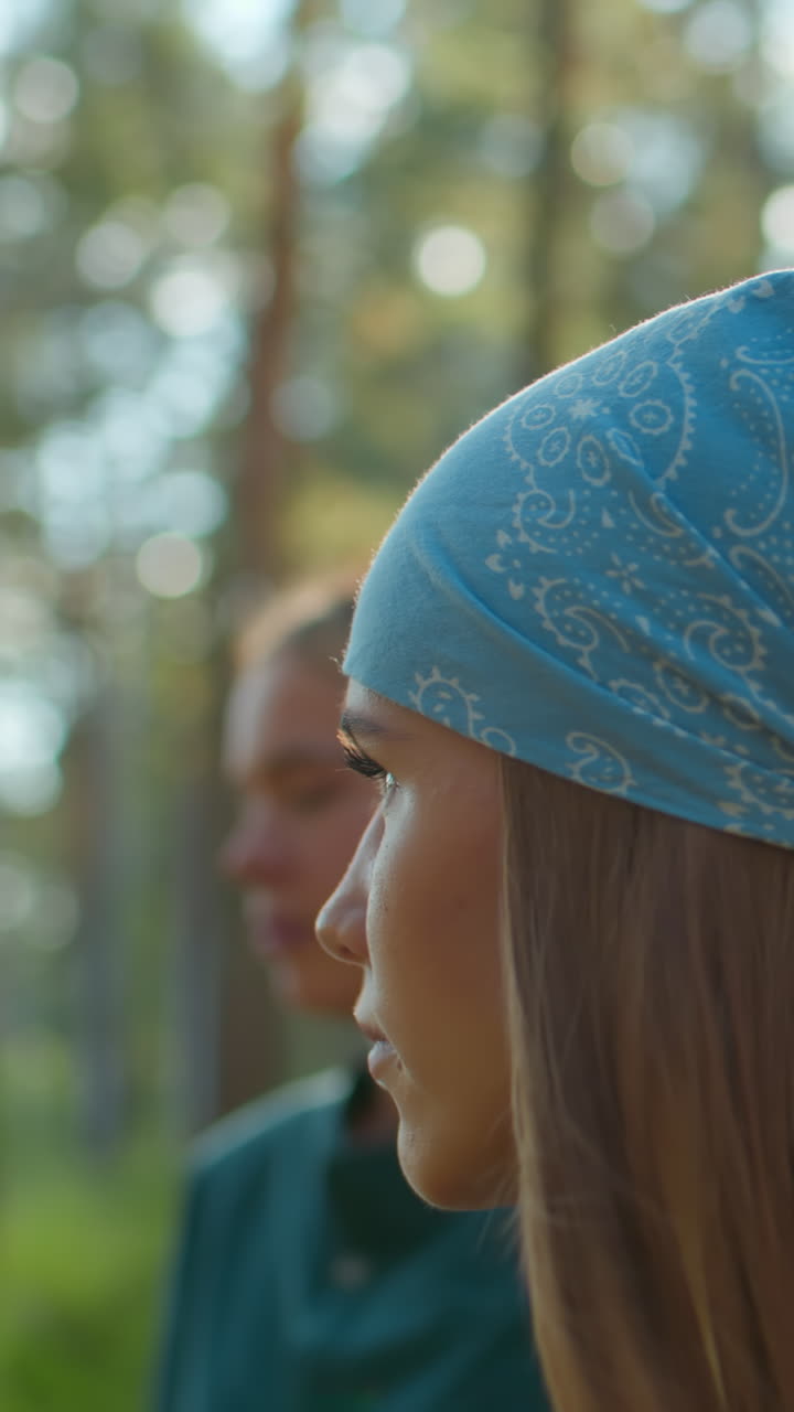 amigos caminando a través de un bosque verde exuberante con una que lleva una bufanda azul, iluminada por la luz del sol que se refleja en su cabello, la dama con la camiseta verde se difumina suavemente en el fondo