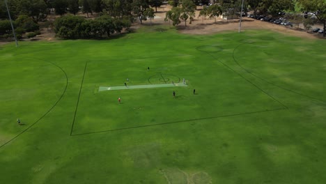 Boys-practice-cricket-on-Perth-City-training-field-in-Australia,-aerial-circling-view