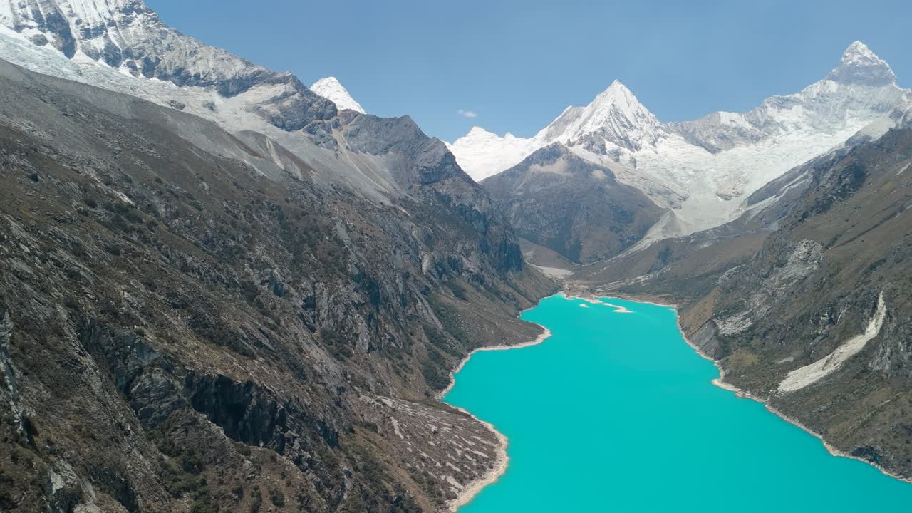 A stunning, high-altitude aerial shot slowly pans to reveal the vast, vibrant turquoise waters of Laguna Parón and the spectacular snow-capped peaks of the Andes in Peru