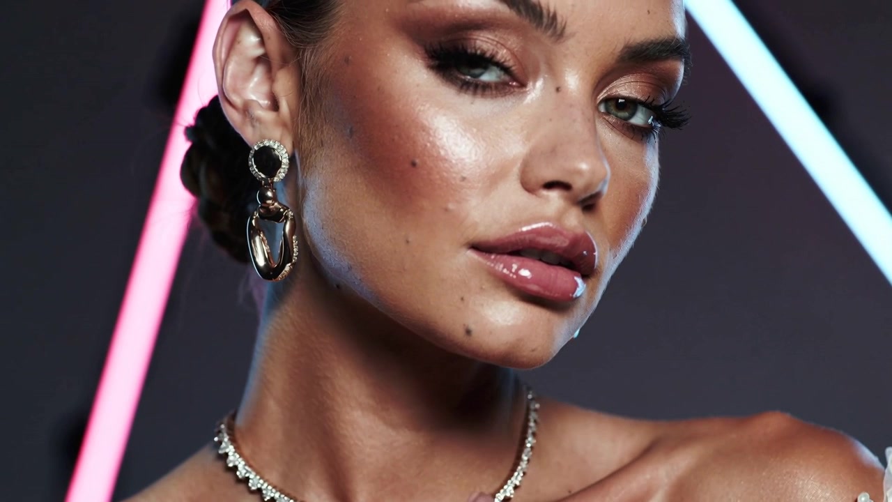 Fotografo che dà indicazioni alla modella che inclina la testa, toccandosi il collo, in posa per un servizio fotografico di bellezza con choker, barre al neon