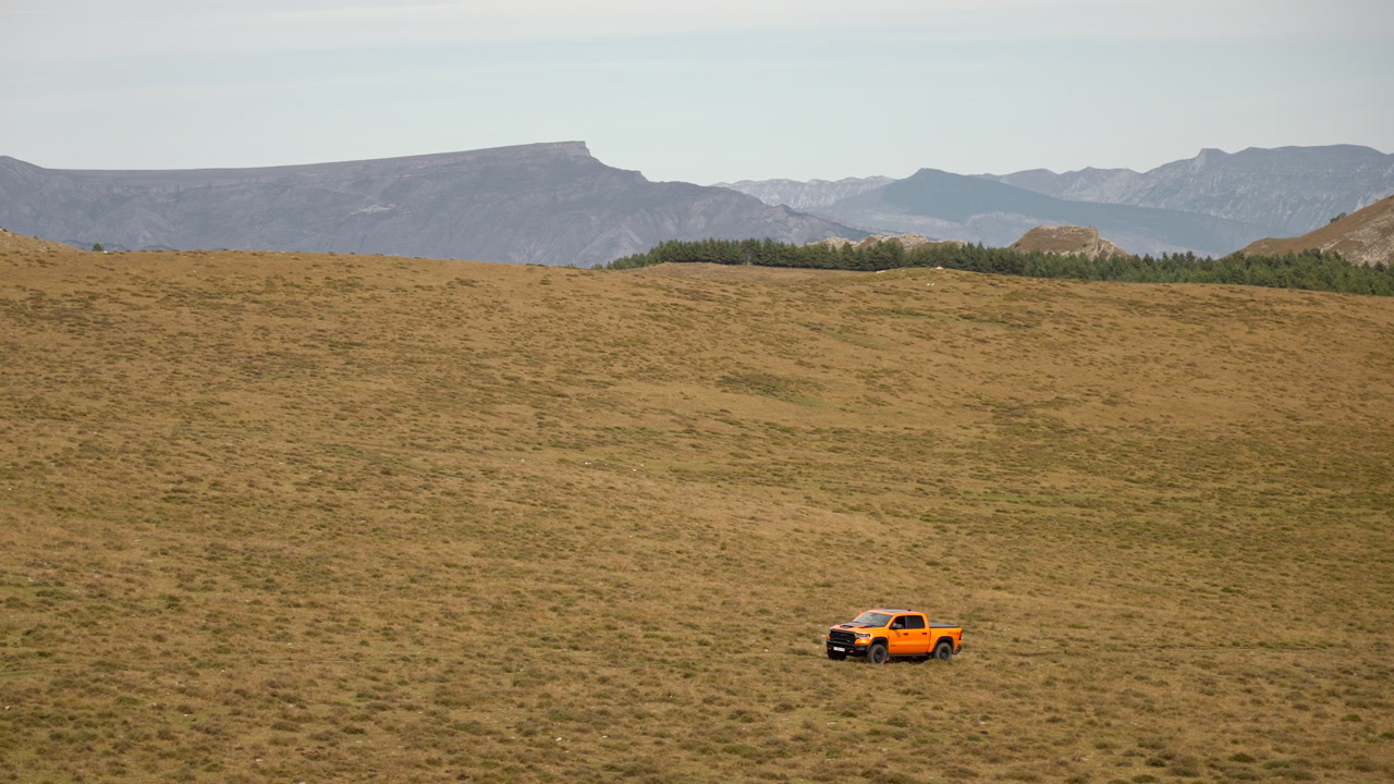 Orange Pickup Crossing Vast Grassland Plain Under Distant Mountains, Lone Vehicle Traverses Dry Prairie. Creative