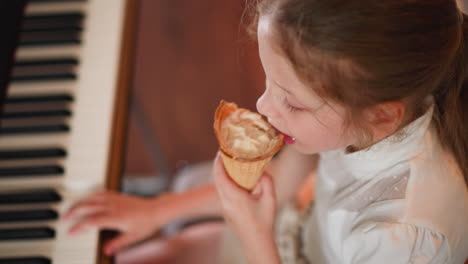 close up top down view of young girl enjoying ice cream cone while lightly pressing piano keys, combining sweet delight with musical play in cozy indoor setting