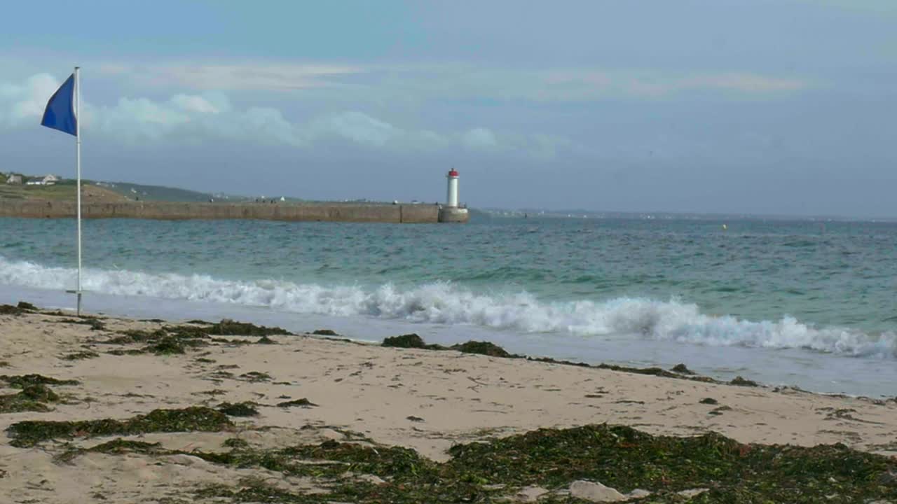 cámara lenta: olas rompiendo en la playa, con un faro en la distancia