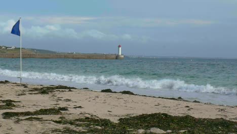 Cámara-Lenta:-Olas-Rompiendo-En-La-Playa,-Con-Un-Faro-En-La-Distancia