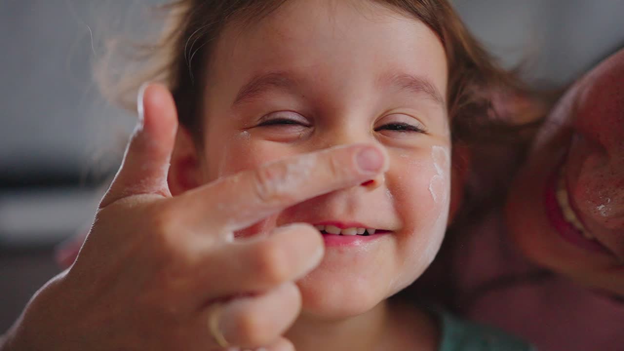 Momenti di gioia: una tenera interazione tra un genitore e il suo bambino mentre si mettono giocosamente la crema, che mostra pura felicità e un legame affettivo in un ambiente intimo