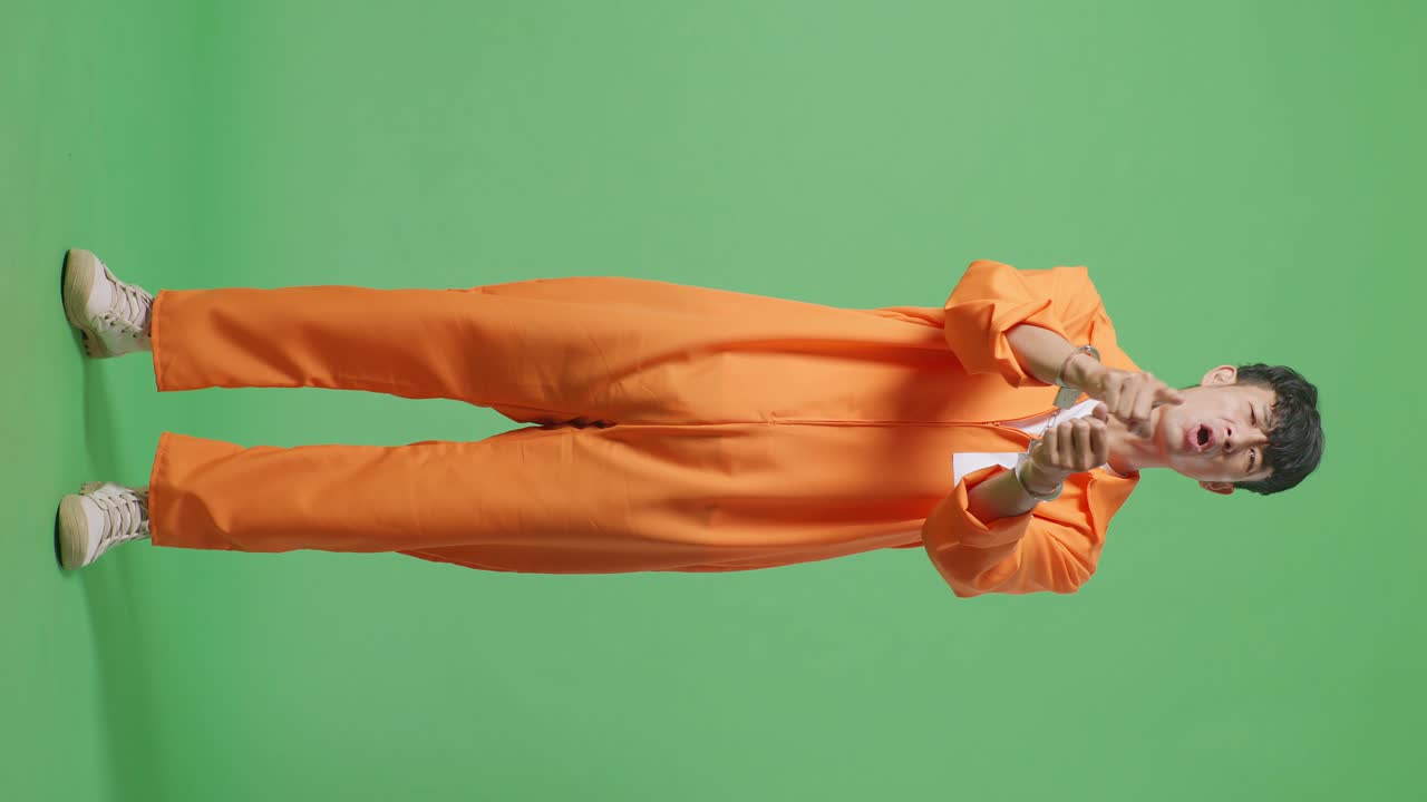 Full Body Of Asian Male Prisoner In Handcuffs Standing On The Green Screen Background, Pointing His Finger Towards You, Speaking Against And Blaming You