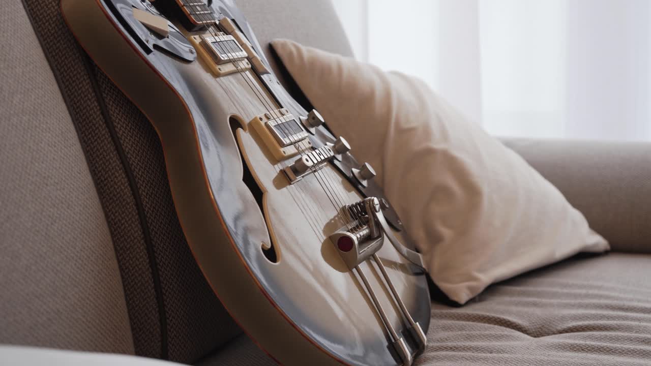 Semi acoustic electric guitar on sofa in empty living room, no people, closeup view