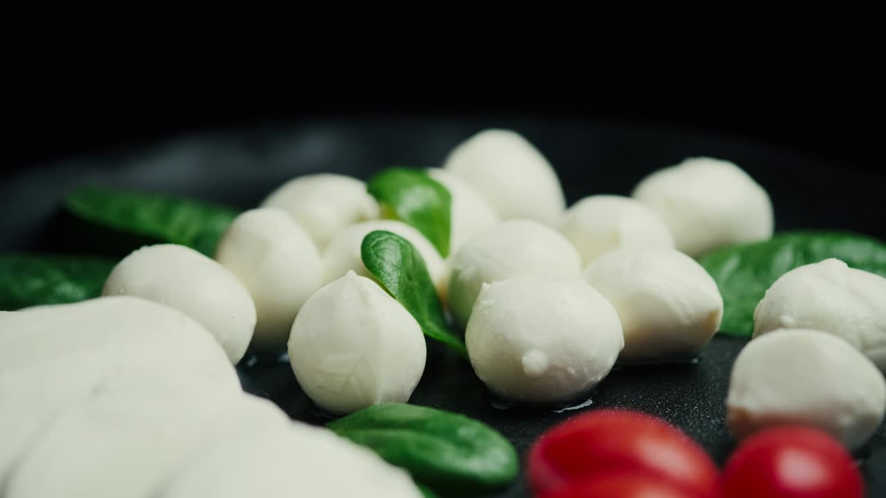 pequeñas bolas de queso mozzarella blanco, hojas de espinaca y tomates en un plato negro.