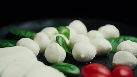 white small mozzarella cheese balls, spinach leaves and tomatoes on black plate. dolly-in shot