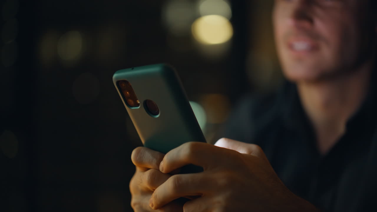 Primo piano di un uomo sorridente che chatta al cellulare di notte a casa. Uomo felice che invia messaggi