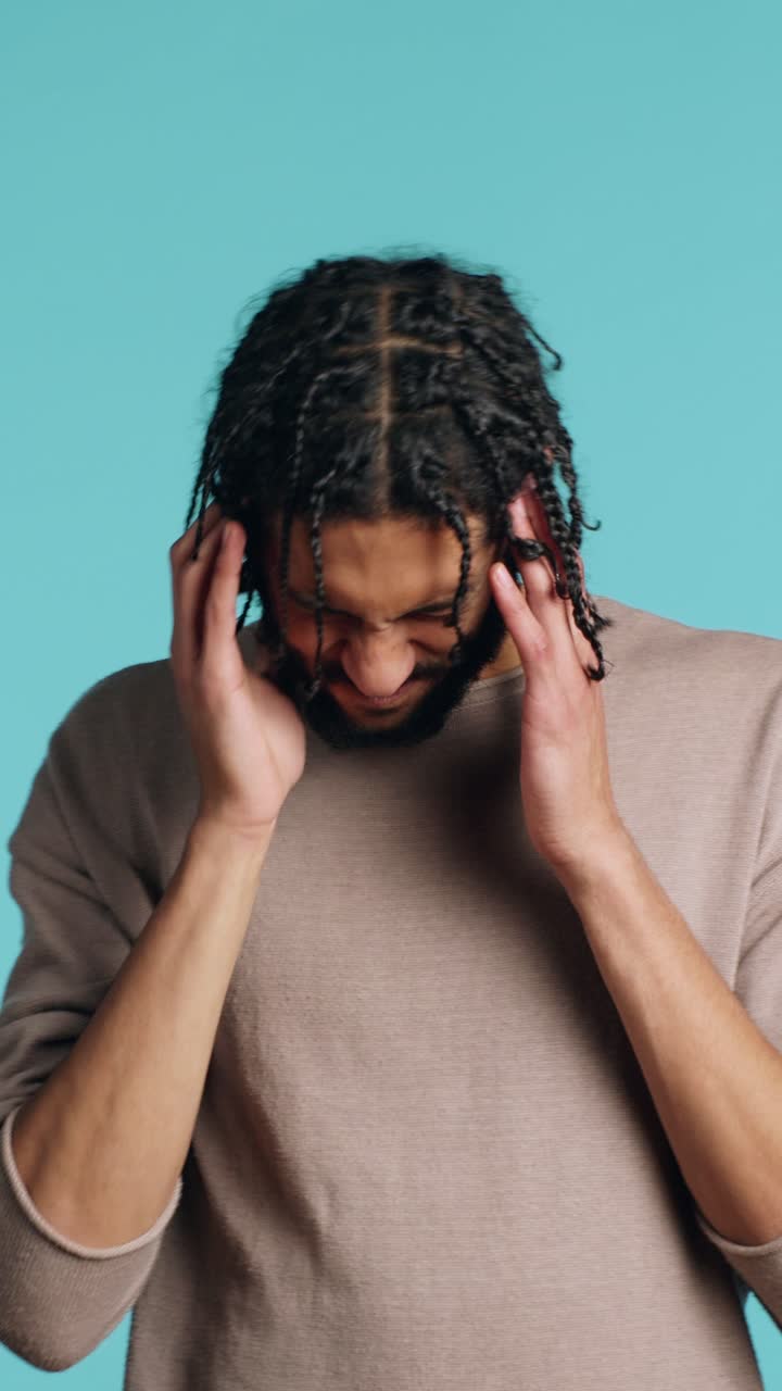Vertical video Man wincing from pain, suffering from headache, studio background
