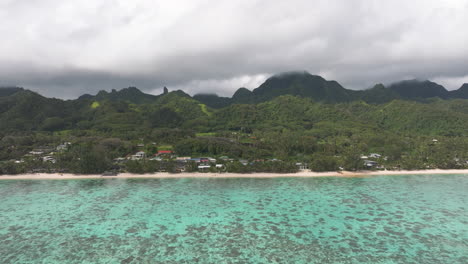 aerial tracking left above coastline and homes built up below mountains in cook islands rarotonga
