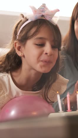 girl blowing out the candles on her birthday cake sitting on a sofa