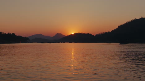 sunset over a river with mountains and boats