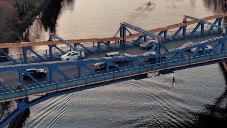 cars drive along the fremont bridge above the fremont cut while rowers paddle below them on the water at golden hour in seattle