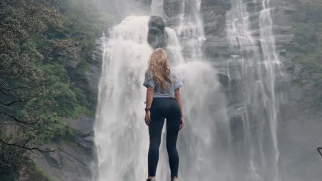a woman stands in awe before the roaring bomburu ella waterfalls, surrounded by mist, jungle, and rocky cliffs in the lush highlands of nuwara eliya, sri lanka.