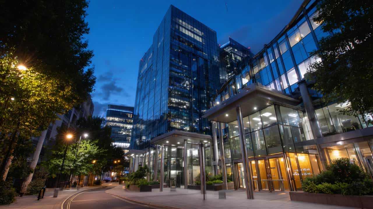 Moderno edificio per uffici urbano di notte con facciata in vetro illuminata e dintorni lussureggianti, che mette in mostra un'atmosfera di professionalità e innovazione