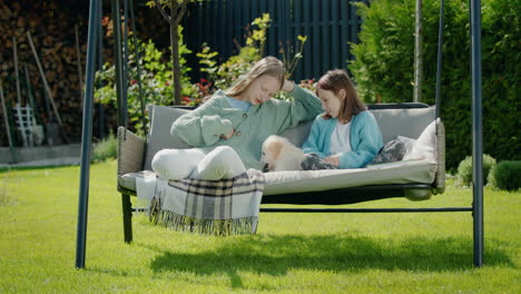 two girls playing with a puppy, sitting on a swing in the backyard of the house