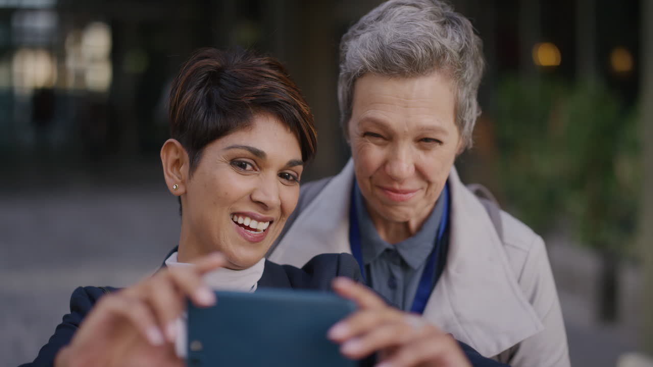 retrato de dos mujeres maduras tomando una foto selfie usando un teléfono inteligente haciendo caras disfrutando de divertirse juntas en la ciudad en cámara lenta relajadas despreocupadas