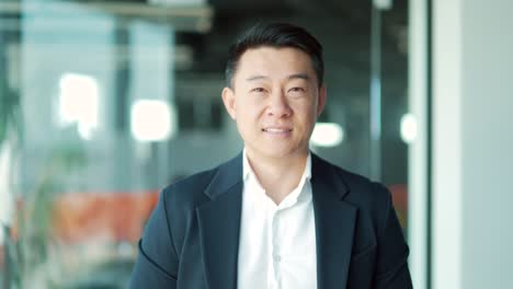 close up portrait confident successful happy asian business man in formal suit looking at camera and smiling indoors modern office. face male businessman worker,