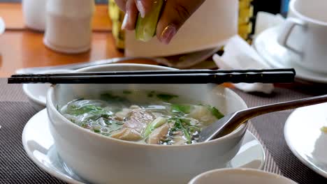 person squeezing lime into a bowl of pho