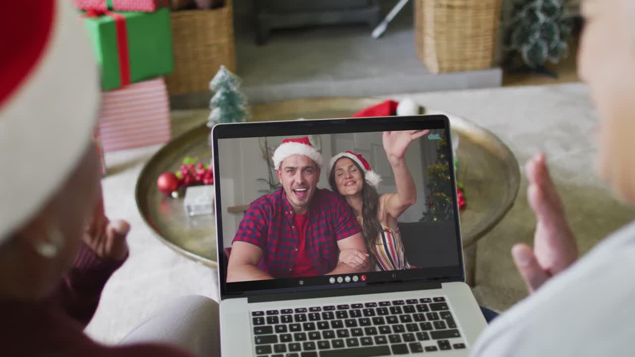 diversas amigas mayores agitando y usando una computadora portátil para una videollamada de navidad con la pareja en la pantalla