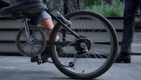 male legs riding bicycle in black shoes at downtown close up. rear wheel view.