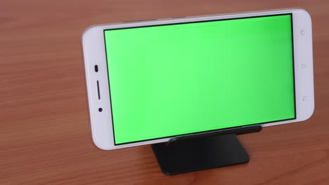 el movimiento deslizante del teléfono de pantalla verde se coloca sobre un pedestal en una mesa de madera