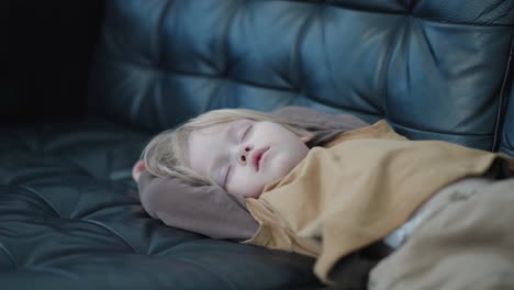 witness the restful nap of a 3-year-old caucasian boy in a medium shot, as he sleeps serenely on a black leather couch