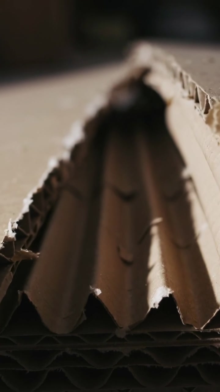 Vertical video: Camera moving forward over packaging board showing torn flutes and fibers for QC