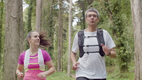 happy man and woman running in forest and talking