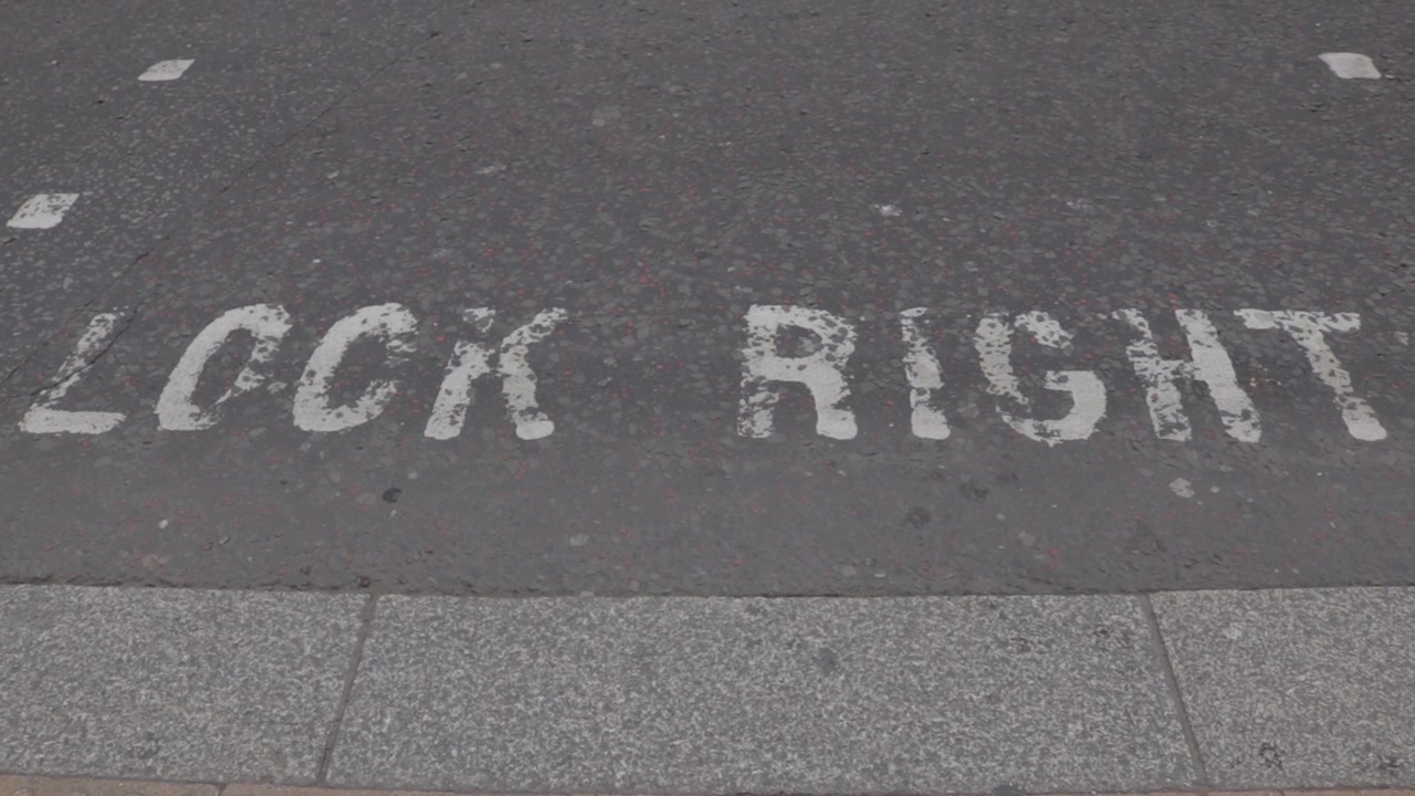 A steady, high-angle shot of the white "LOOK RIGHT" warning painted on black asphalt in London. This safety sign helps pedestrians navigate traffic in the UK where vehicles drive on the left side.