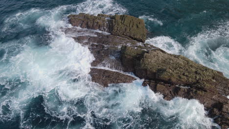 aerial view of sea waves crashing on rocks on a sunny day