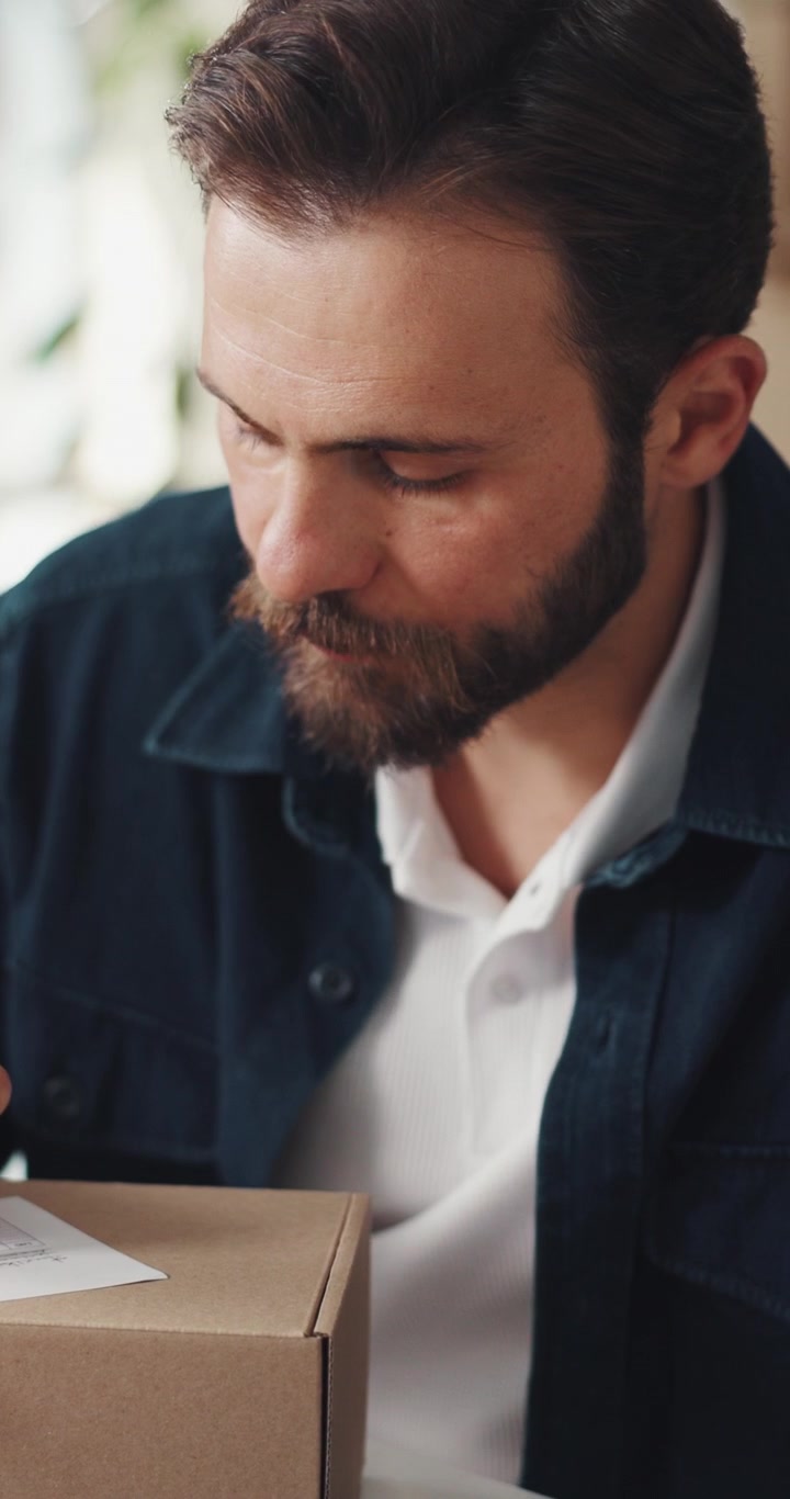 Bearded Man Writing on a Package and Using a Tablet