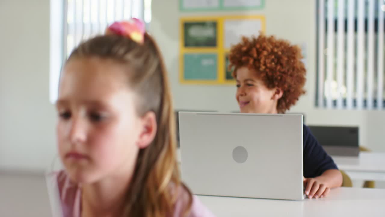 Compagni di classe, ragazze e ragazzi, concentrati sui computer portatili in classe mentre l'insegnante dà un suggerimento che fa sorridere un ragazzo