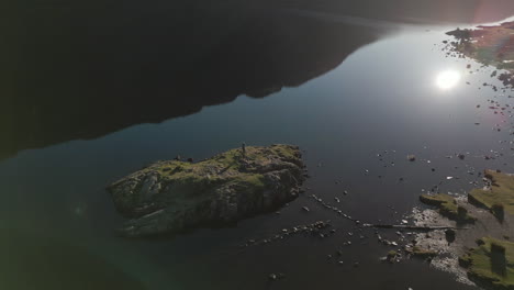 small island orbit in bright sunshine with dark water and mountain reflections at wastwater lake district uk