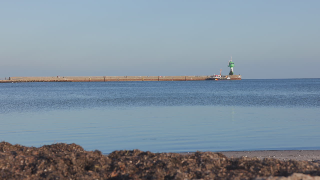 Peaceful seaside view in Luebeck-Travemuende with a long pier, green lighthouse, and calm blue water under a clear sky — tranquil coastal atmosphere