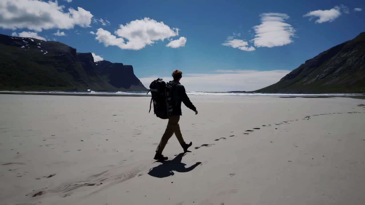 Backpacker Walking on a Vast Remote Beach with Mountains and Blue Sky