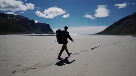 backpacker walking on a vast remote beach with mountains and blue sky