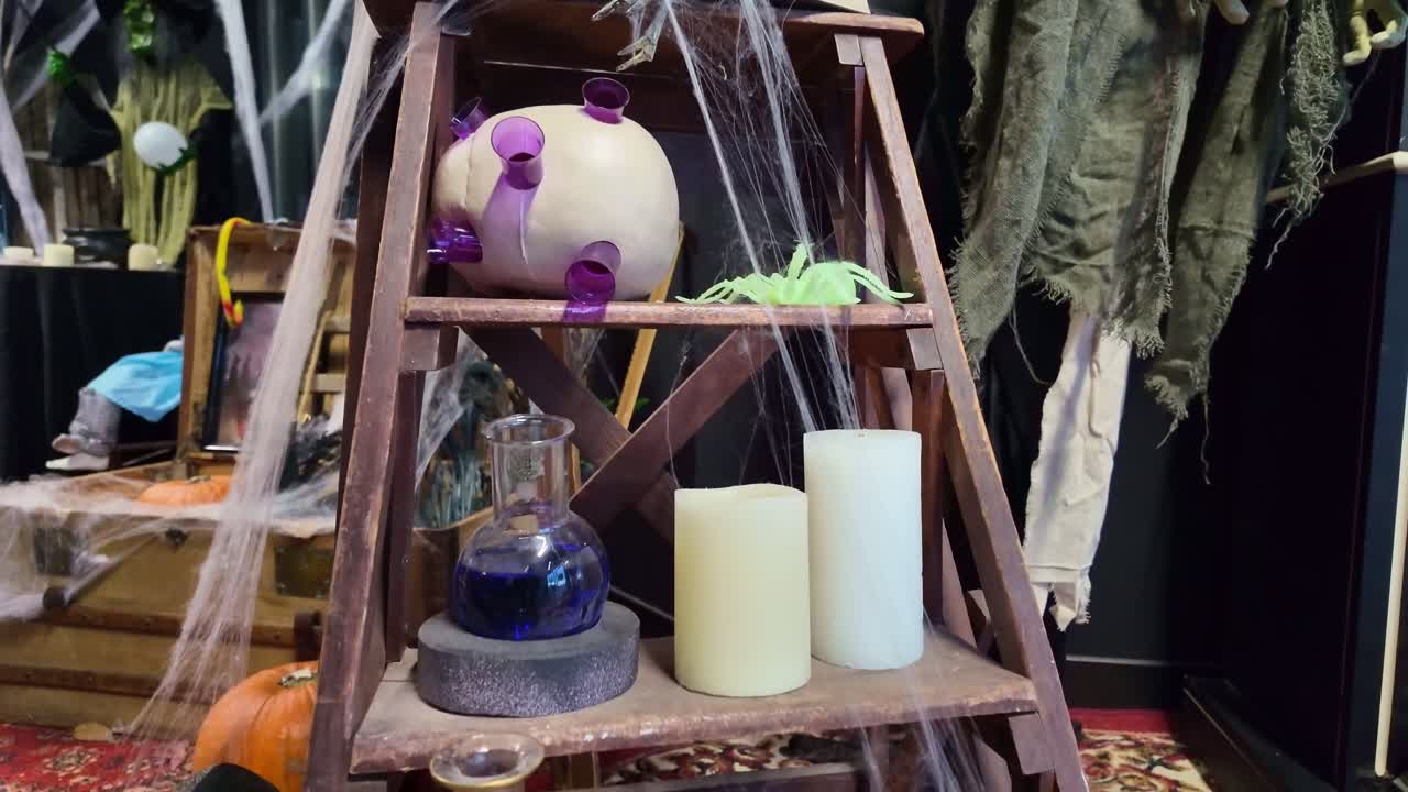 Camera tilts down over Halloween decorations showing skulls, candles, spider webs, potions and pumpkins