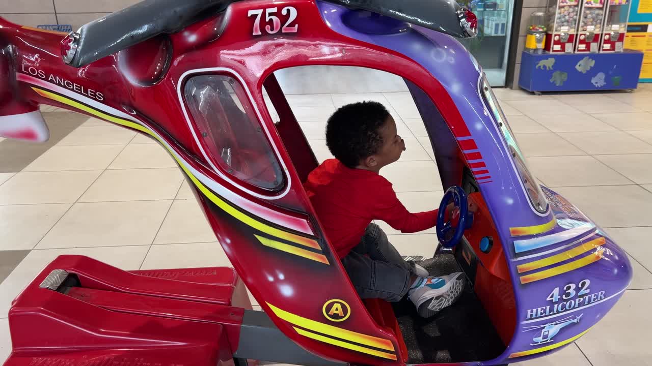 niño negro de 3 años disfrutando de un paseo con monedas en un helicóptero de juguete en un centro comercial