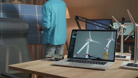 laptop showing wind turbine on the table while a man walks into the office to look at solar cell